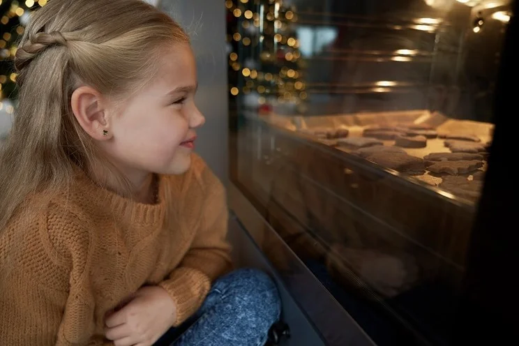 Girl looking into oven as Christmas cookies bake