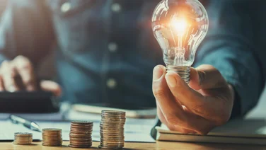 business man hand holding lightbulb with using calculator to calculate and money stack. idea saving energy and accounting finance in office concept