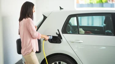 woman plugging in a charger to an electric vehicle in a garage