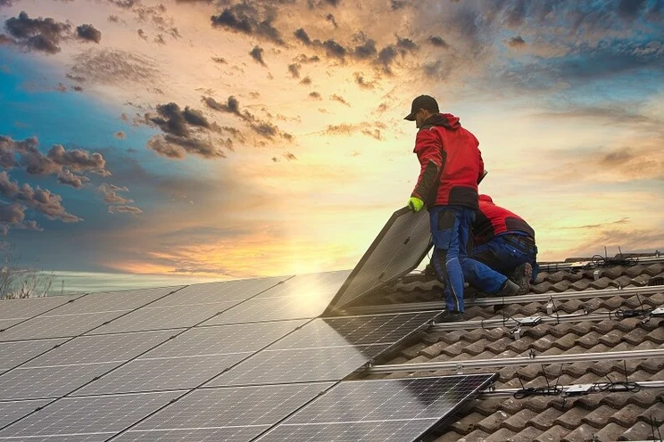 Two men installing solar panels on the roof of a house, with a sunset sky in the background