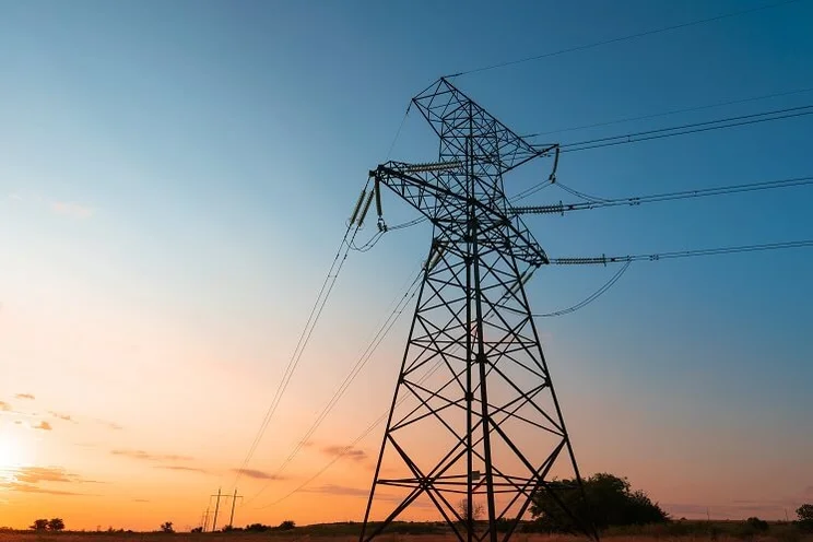 An electricity pylon at dusk, with wires running to another pylon in the distance.